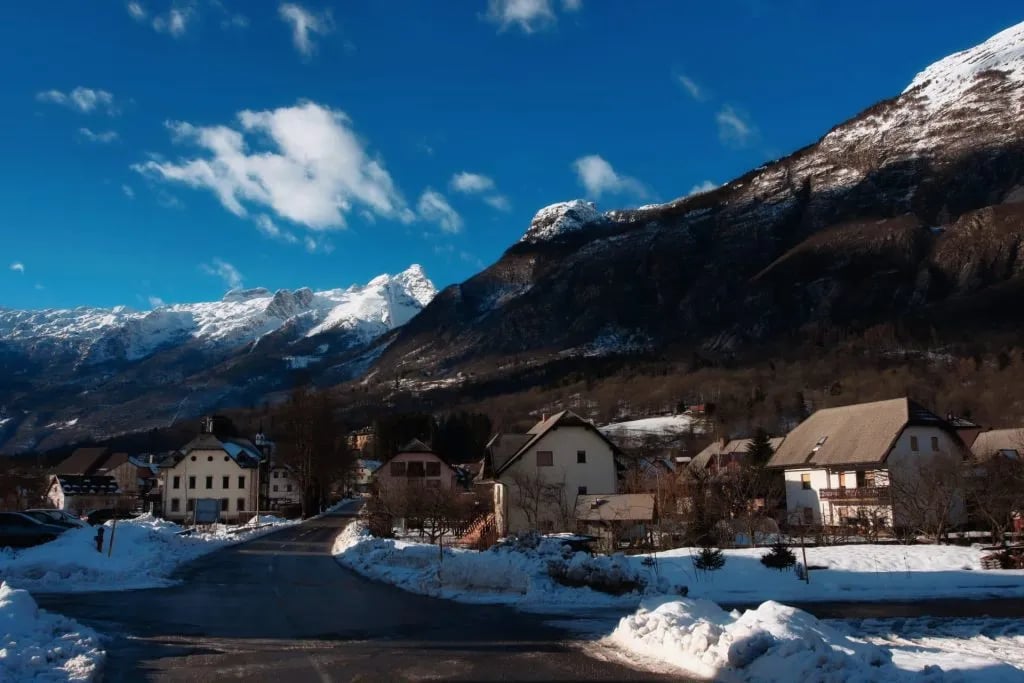 Alpine village in Bovec with snow-covered mountains under a bright blue sky in winter.