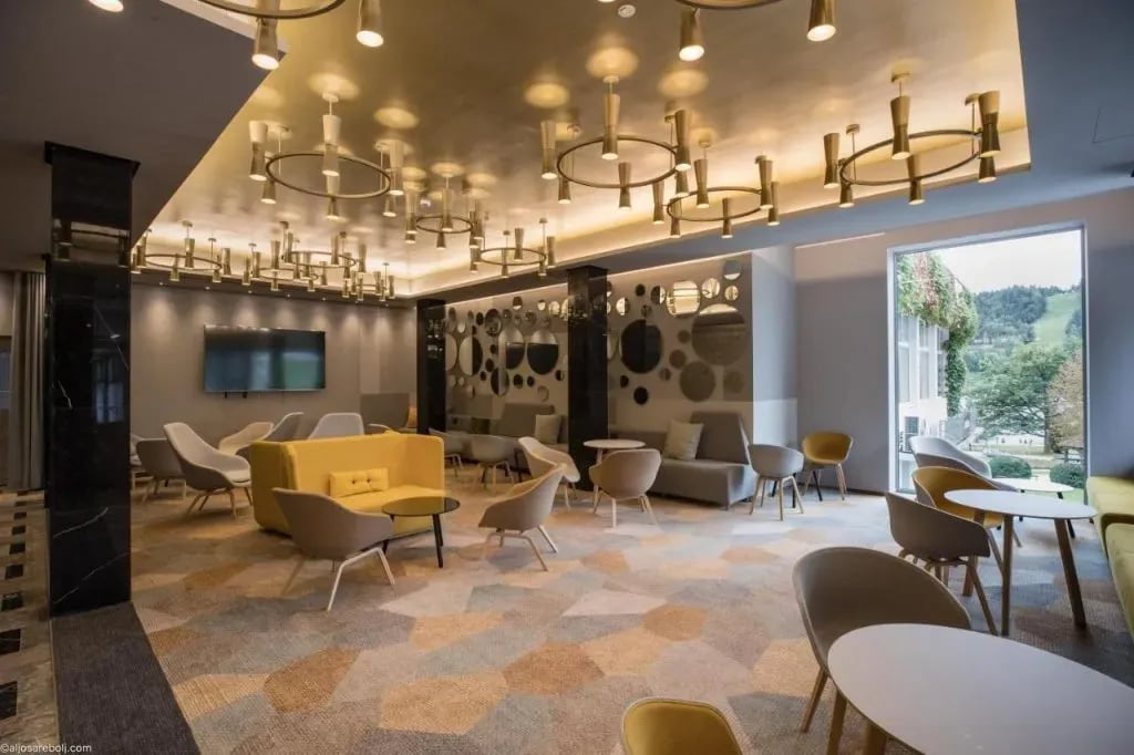 Lounge area with modern seating, geometric carpet, and view of green mountain slope