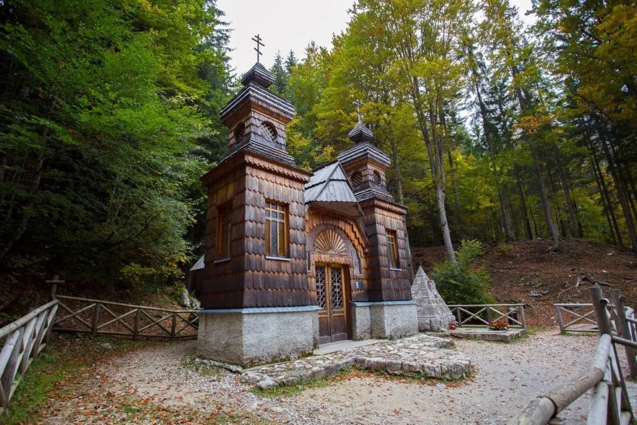 Russian chapel near Vršič Pass with dark wood shingles surrounded by autumn forest.