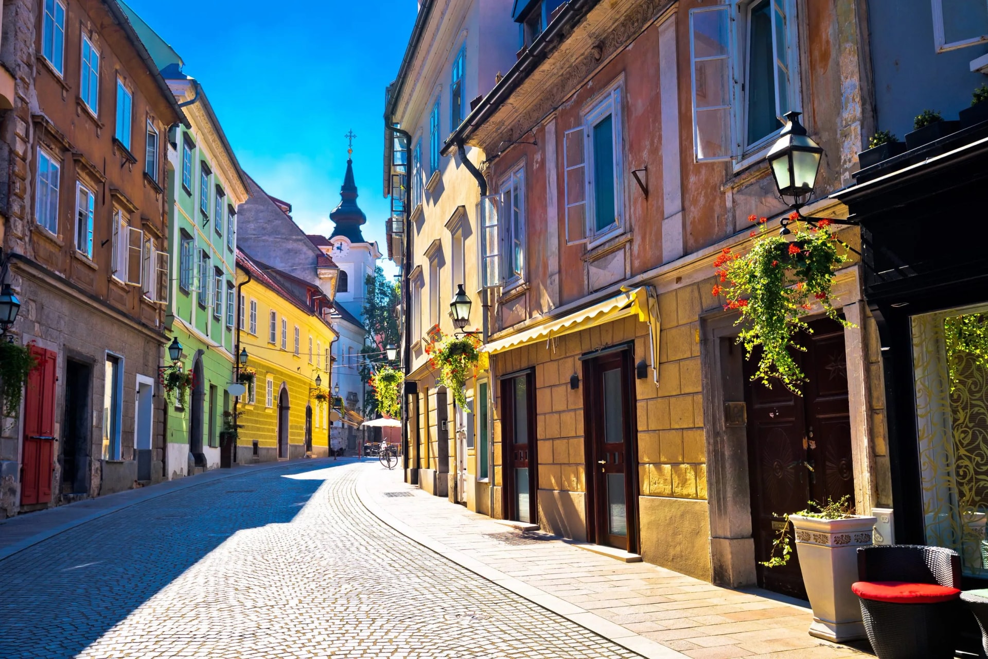 Cobblestone street in Ljubljana Old Town with colorful buildings and a church spire.