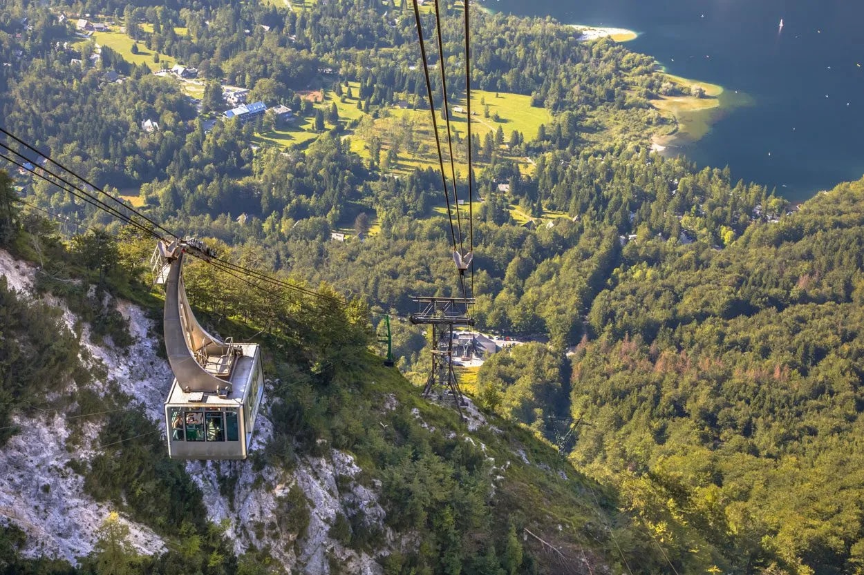 Cable car ascending above Vogel overlooking Bohinj lake and dense green forest.