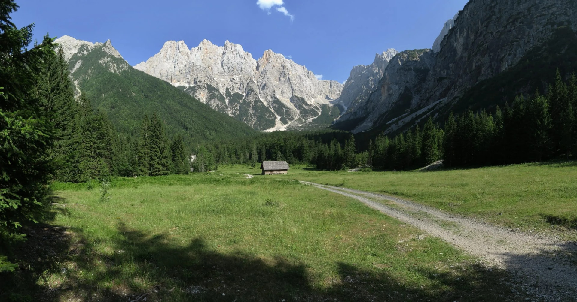 Krnica Valley with the top of Mount Križ, green meadow, and wooden hut.