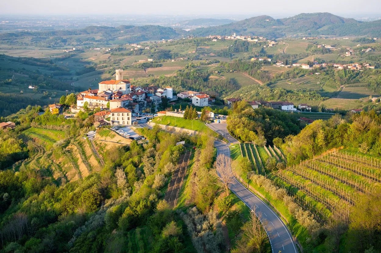 Goriška Brda village perched on a hill surrounded by green vineyards and rolling hills.