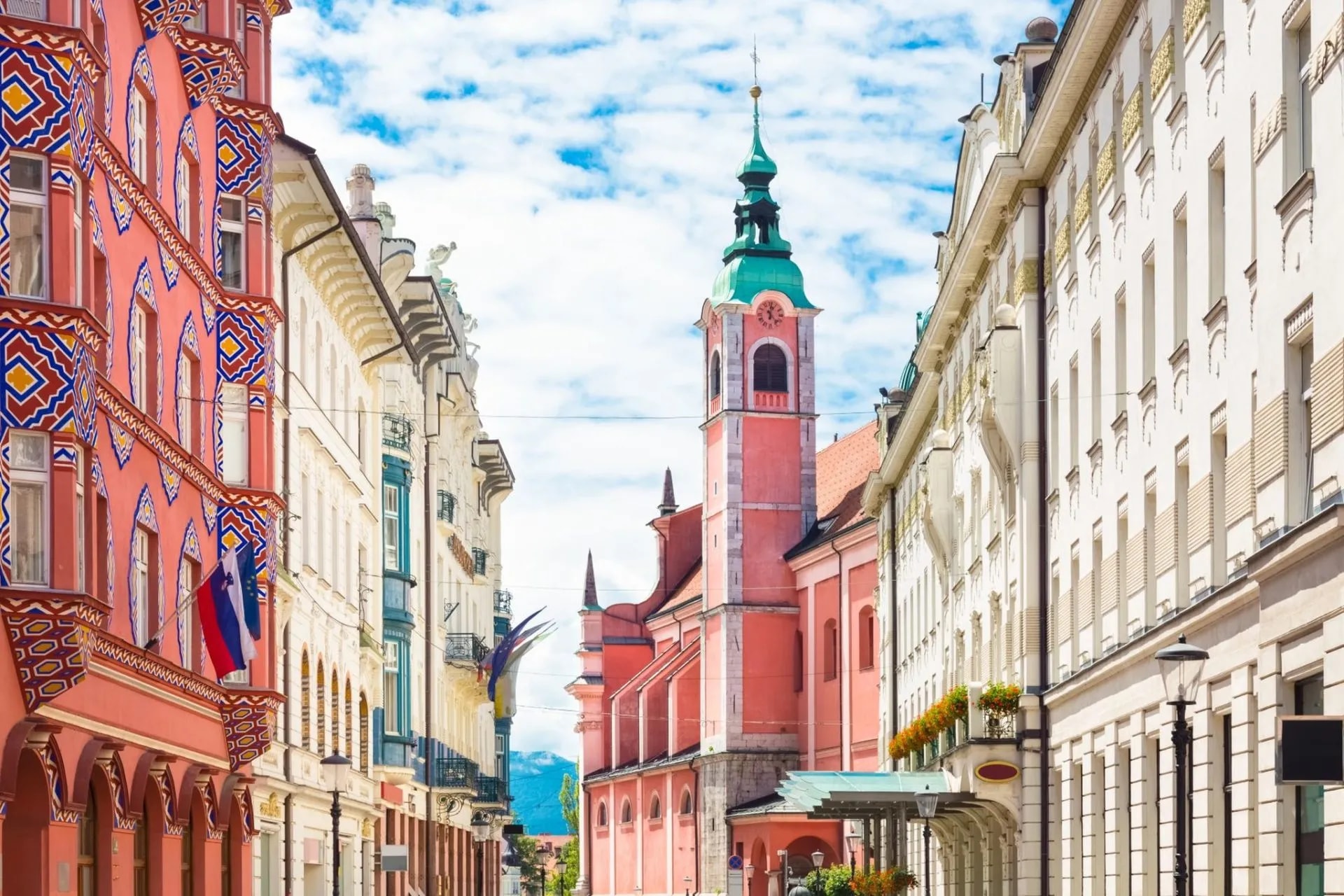 Colorful historic buildings line a street leading to the pink Franciscan Church in Ljubljana.
