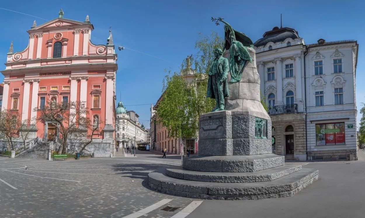 Preseren statue in Ljubljana square with pink Franciscan Church and white historic building.