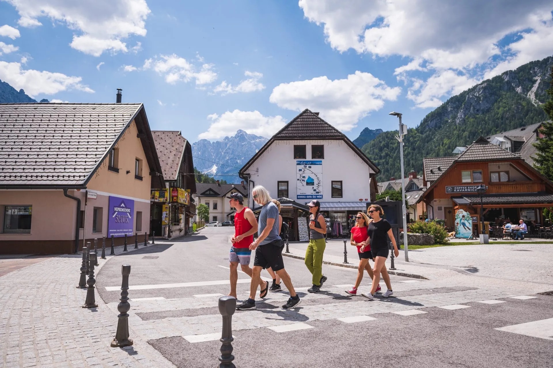 Group walking across a crosswalk in Kranjska Gora village with alpine mountains in the background.