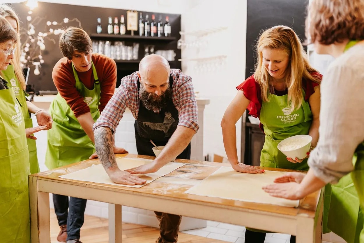 People learning to roll dough during a traditional Slovenian cooking class indoors.