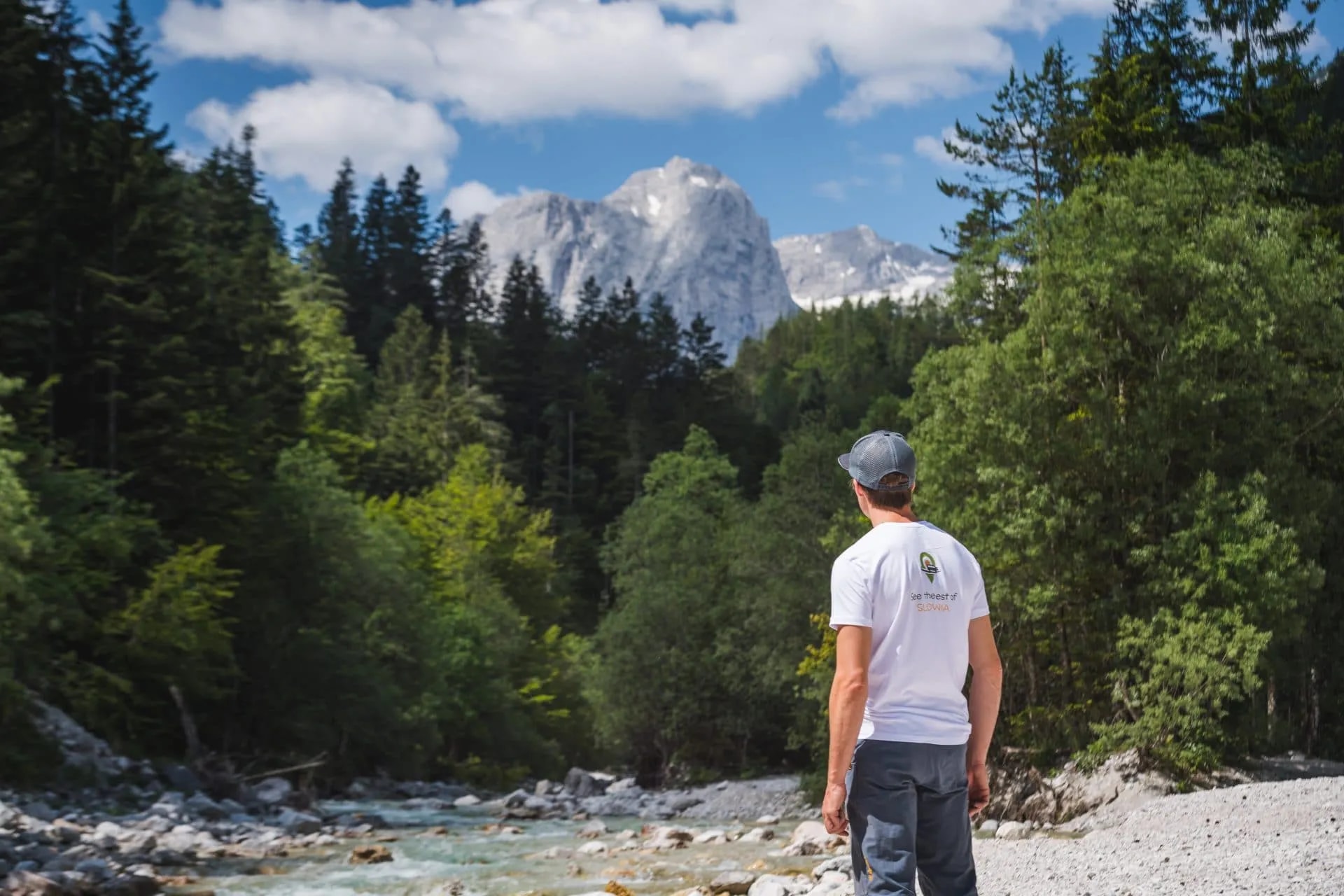 Hiker looking at rocky river and jagged mountain peaks in Vrata Valley, Slovenia