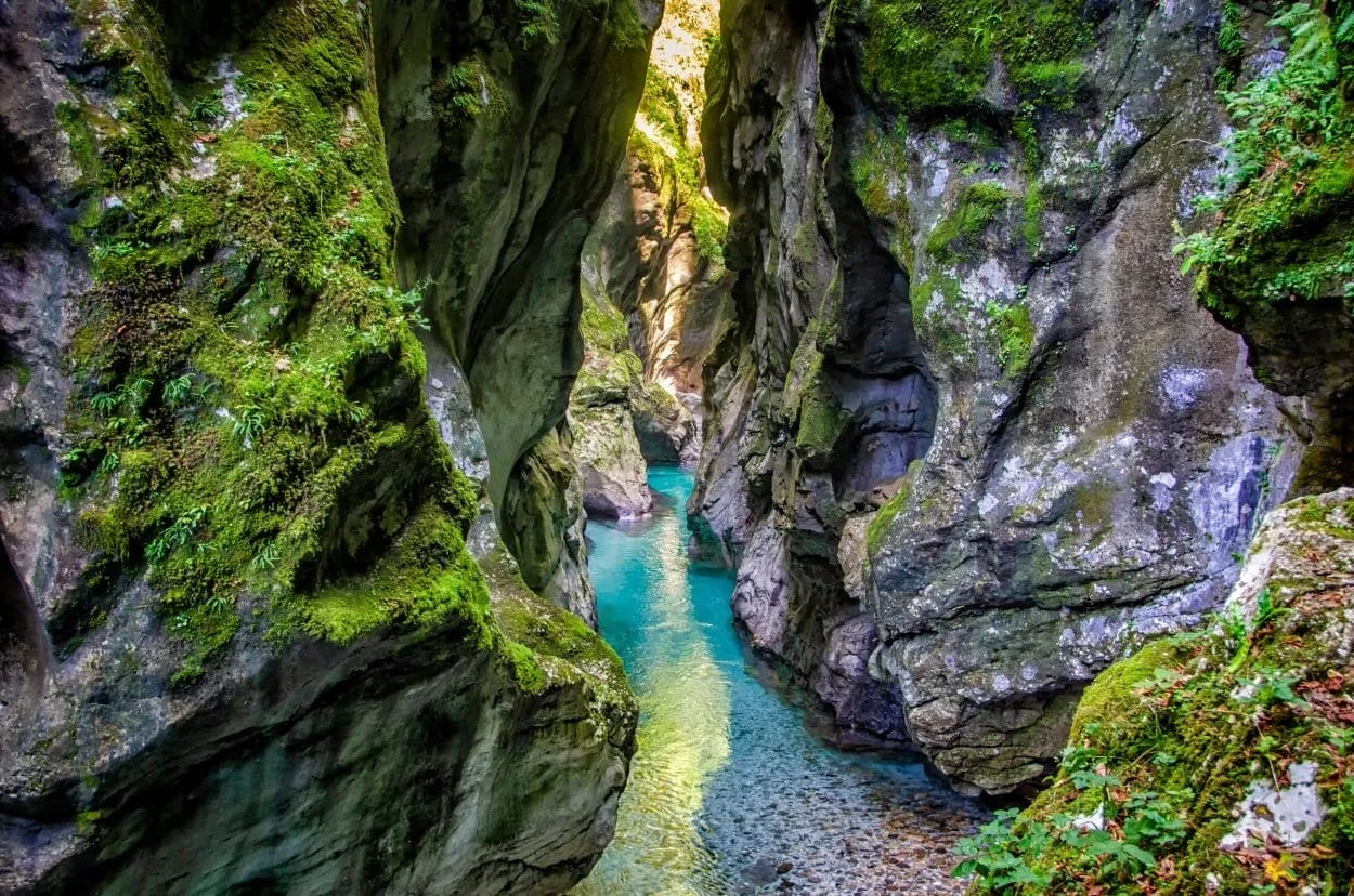 Clear turquoise river flowing through moss-covered rock gorge in Tolmin Gorges.