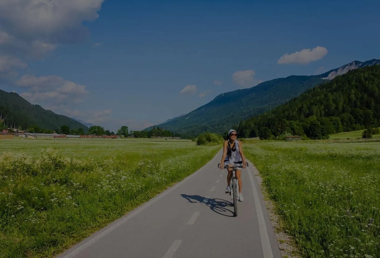 Cycling on a paved path through a green meadow toward mountains near Zelenci.