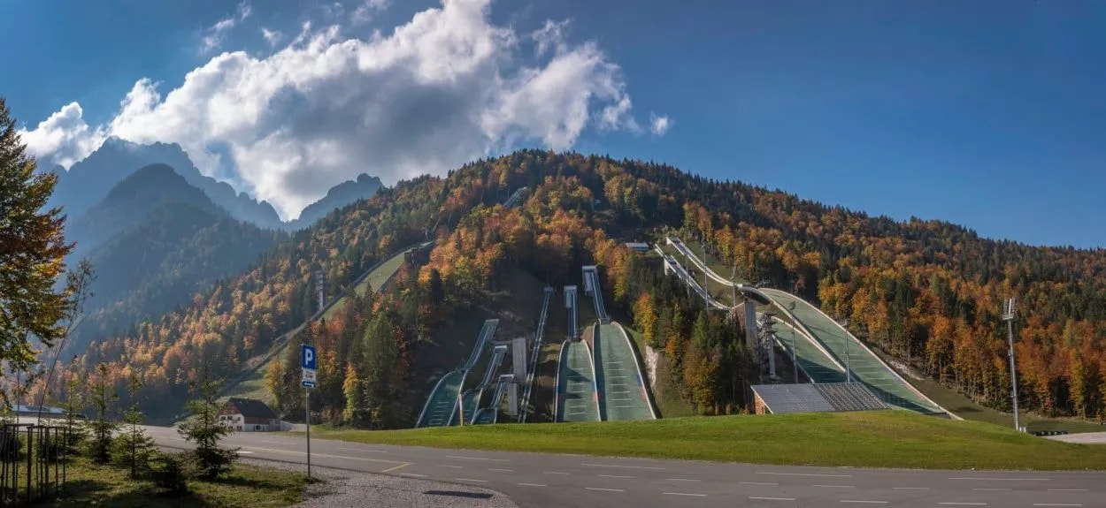 Ski jumping hills with green summer surfaces on a forested mountain in autumn, Planica.