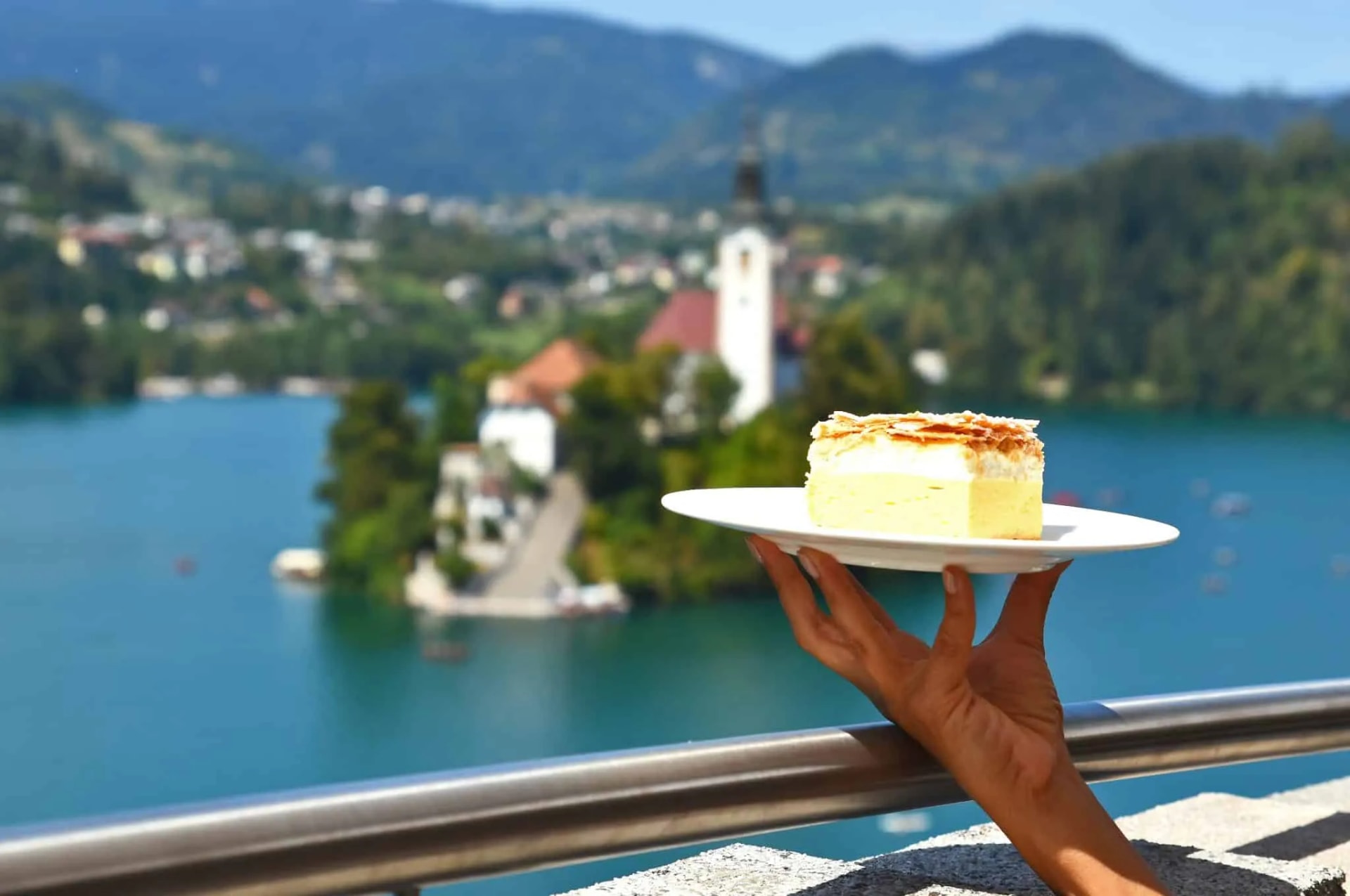 Bled cream cake held over Lake Bled with island church and mountains in background