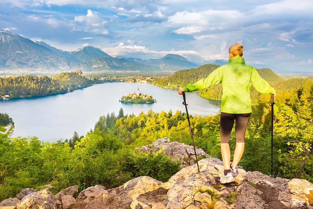 Hiker with poles overlooking Lake Bled island and Julian Alps from a viewpoint