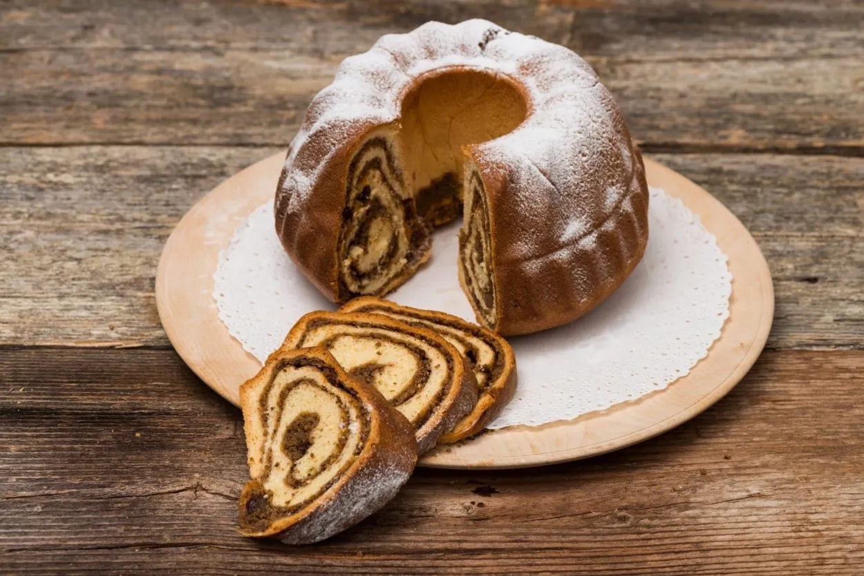Potica nut roll cake dusted with powdered sugar on a wooden board on rustic wood.
