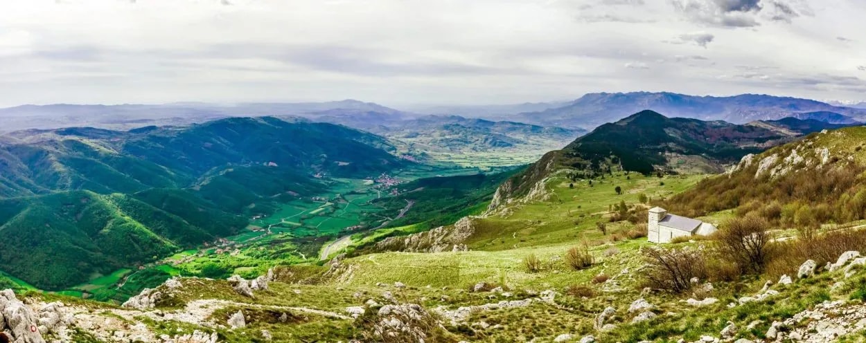 Panoramic view of green mountains, valley, and a small white church in Vipava Valley, Slovenia.