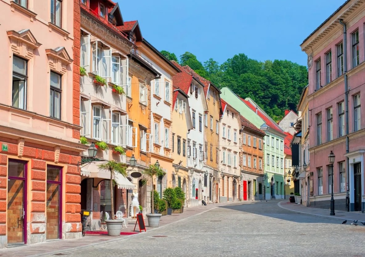 Cobblestone street in Gornji trg, Ljubljana, lined with colorful historic buildings and green hillside.
