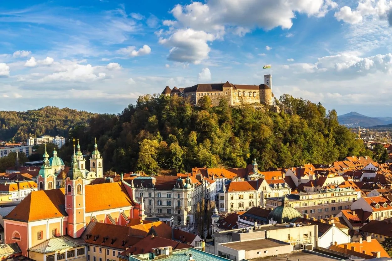 Ljubljana Castle overlooking the city's orange rooftops and church spires under a blue sky.