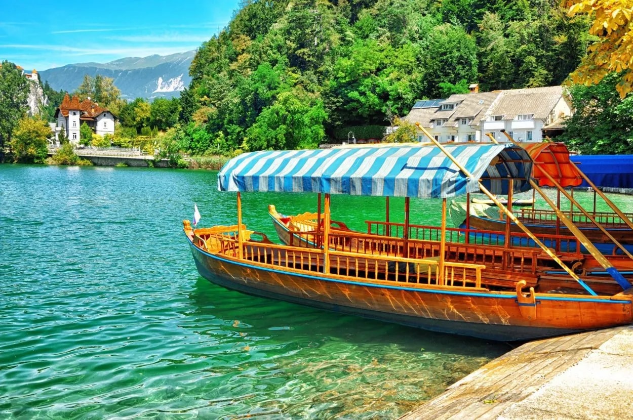 Pletna boat docked on Lake Bled with green water and forested mountains.
