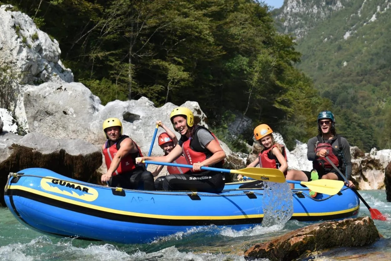 Family white water rafting on a blue inflatable boat in a rocky river canyon.