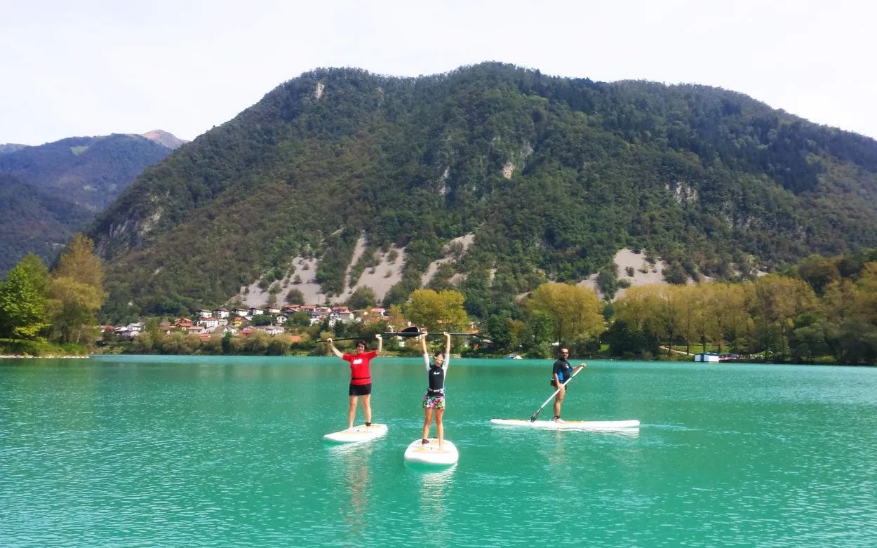Stand-up paddle boarding on turquoise Soca River with forested mountains and village backdrop.
