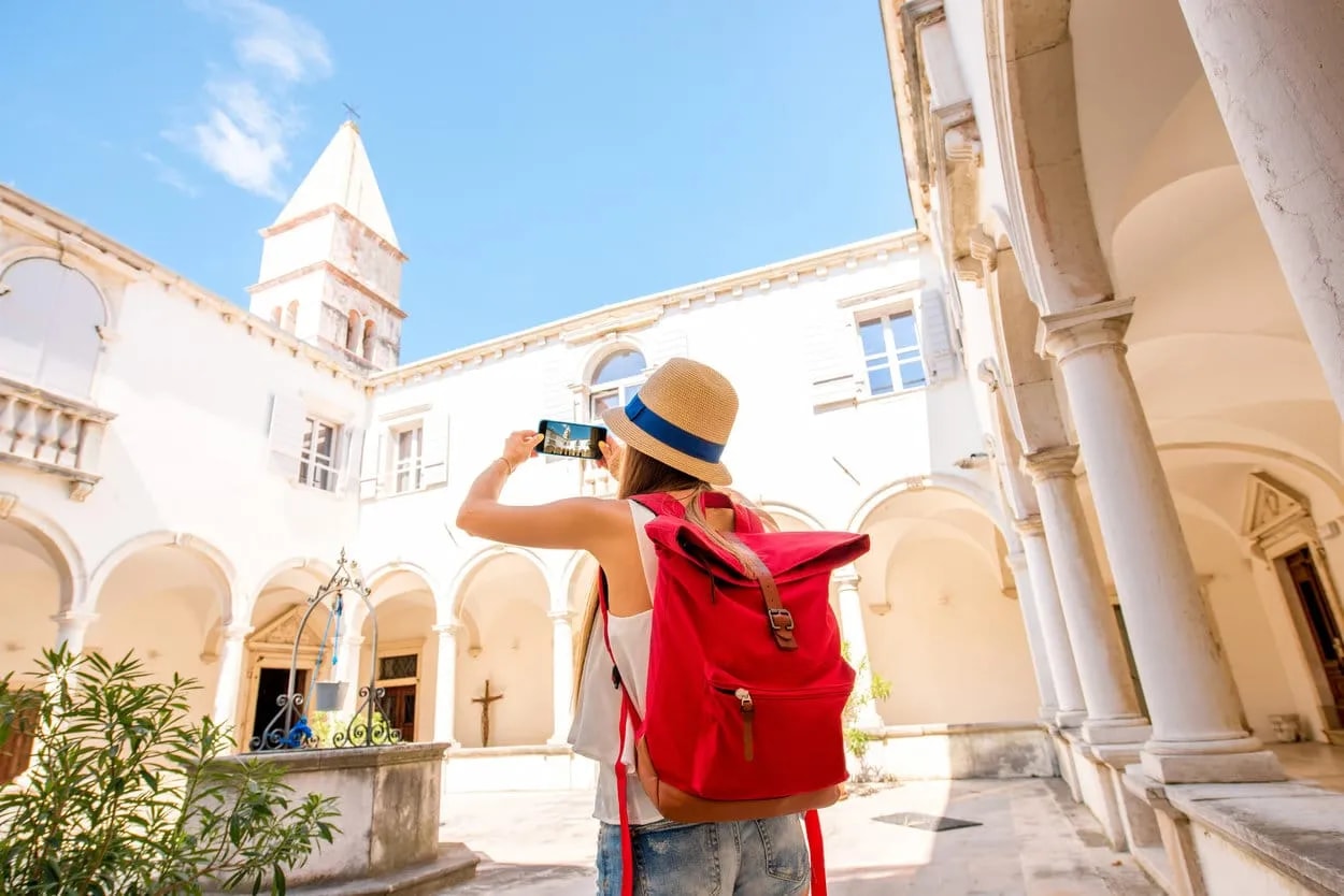 Tourist photographing white cloister with bell tower in Piran on sunny day