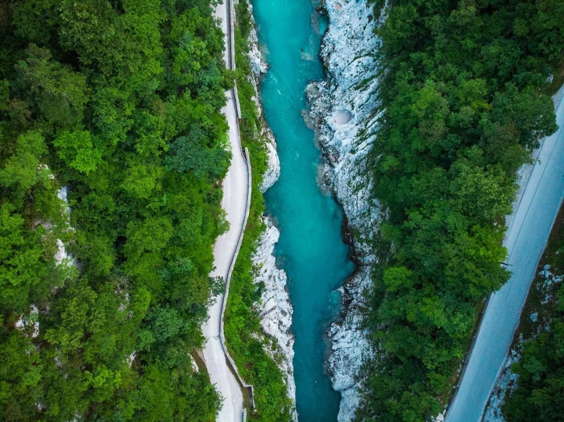 Aerial view of turquoise Soca River canyon with roads winding through dense green forest.