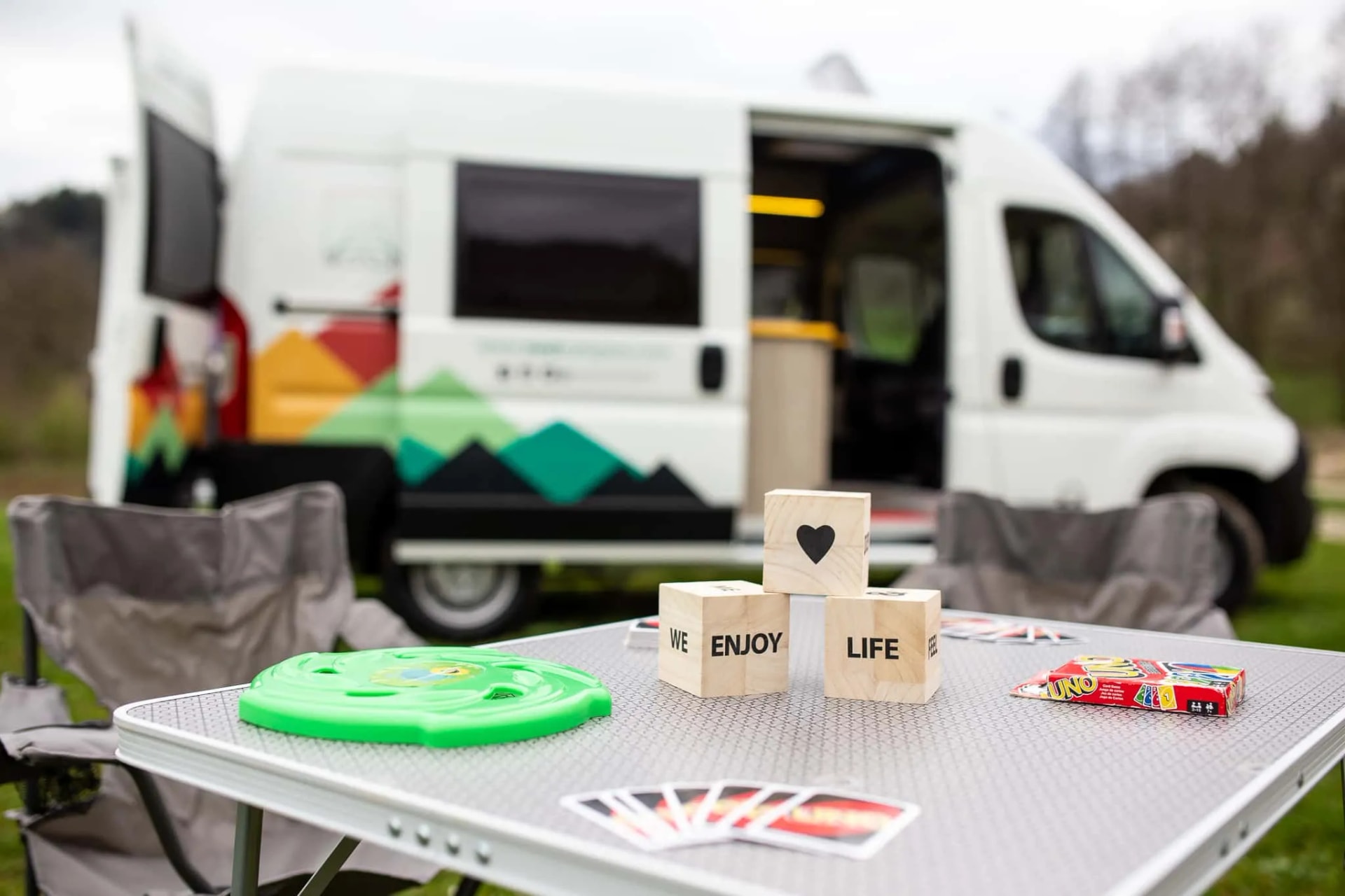 Camping setup with folding table, games, and camper van parked on grass outdoors