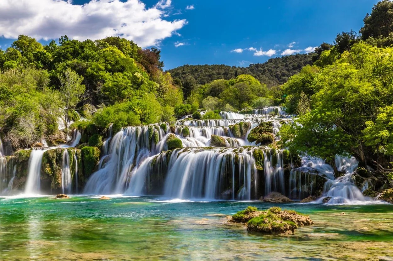 Cascading waterfalls over mossy travertine barriers into turquoise pools at Plitvice Lakes.