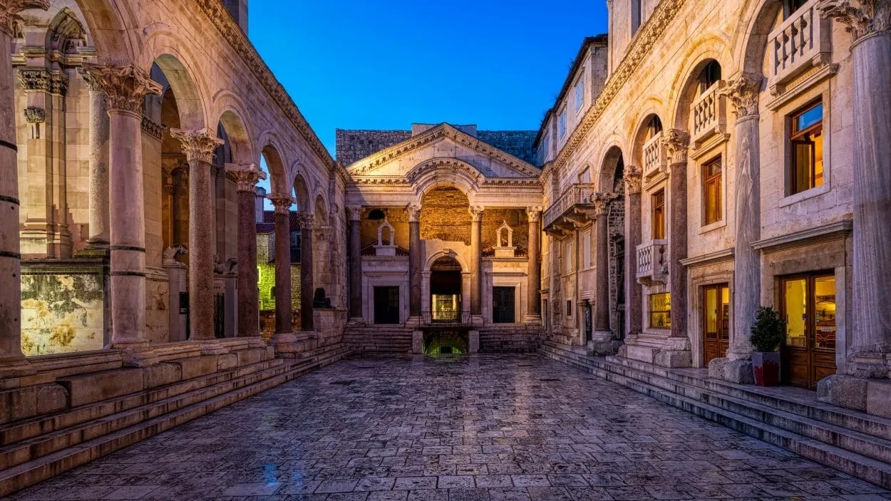 Stone courtyard with Romanesque architecture and illuminated arches at twilight