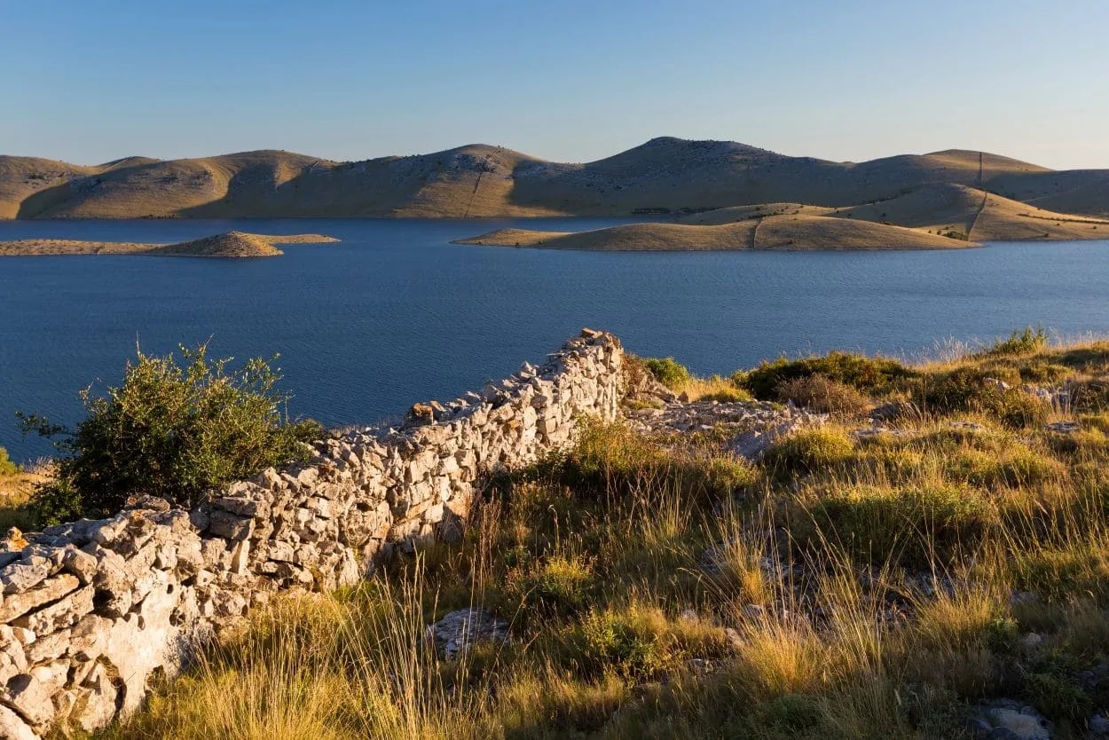 Stone wall overlooking blue water, small islands, and arid hills in Kornati National Park.