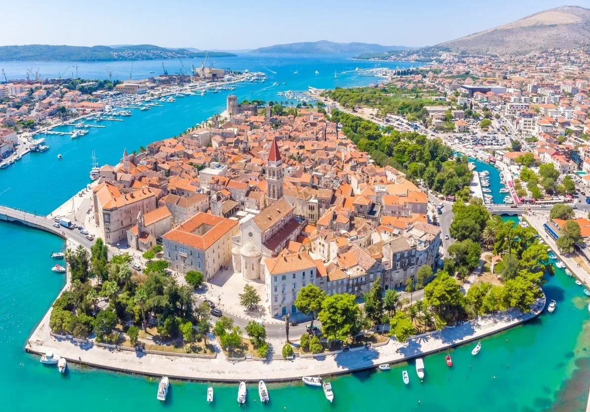 Aerial view of Trogir historic town with orange roofs on a peninsula surrounded by turquoise sea.