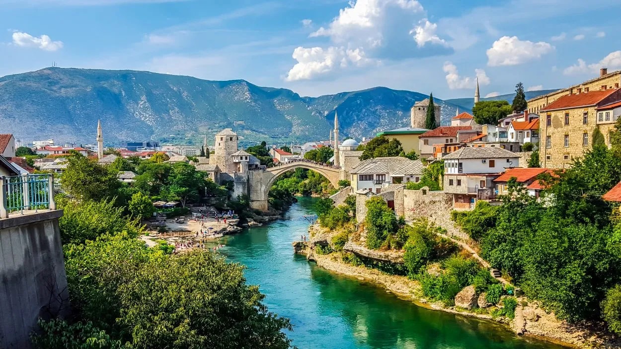 Stari Most bridge over emerald river in Mostar with historic town and mountains.