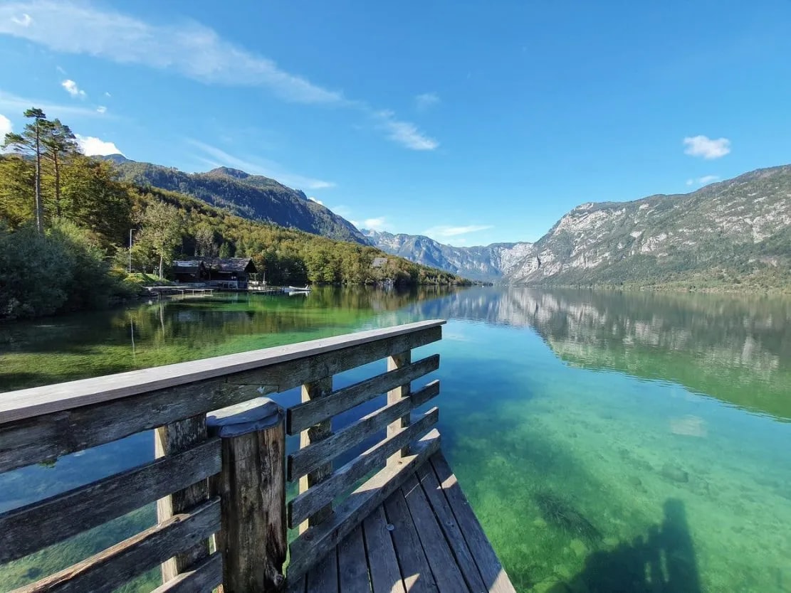 Wooden dock overlooking clear turquoise water of Bohinj Lake with mountains and forest.