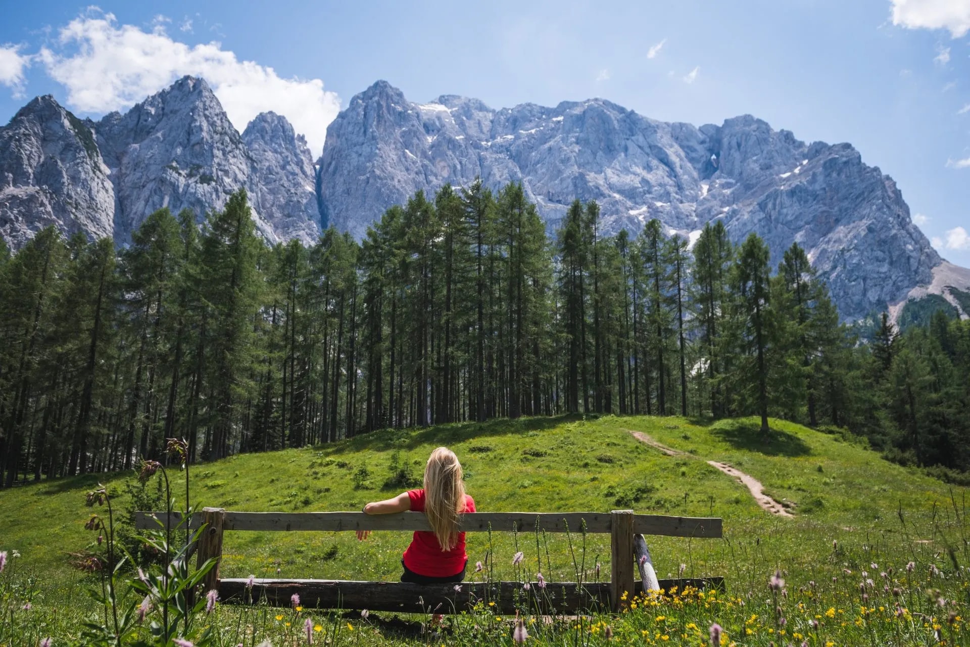 Girl enjoying mountain panorama from a bench at Vršič Pass with green meadow.