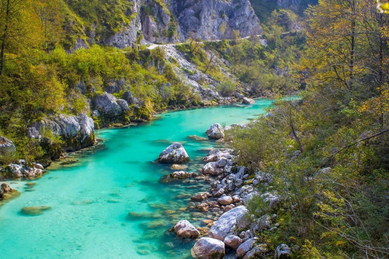 Turquoise river flowing through a rocky gorge with lush green and yellow foliage, likely Soca Valley.