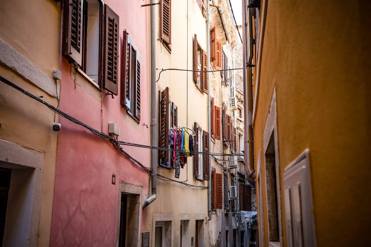 Narrow alleyway in Piran with colorful historic houses, open shutters, and laundry drying outside.