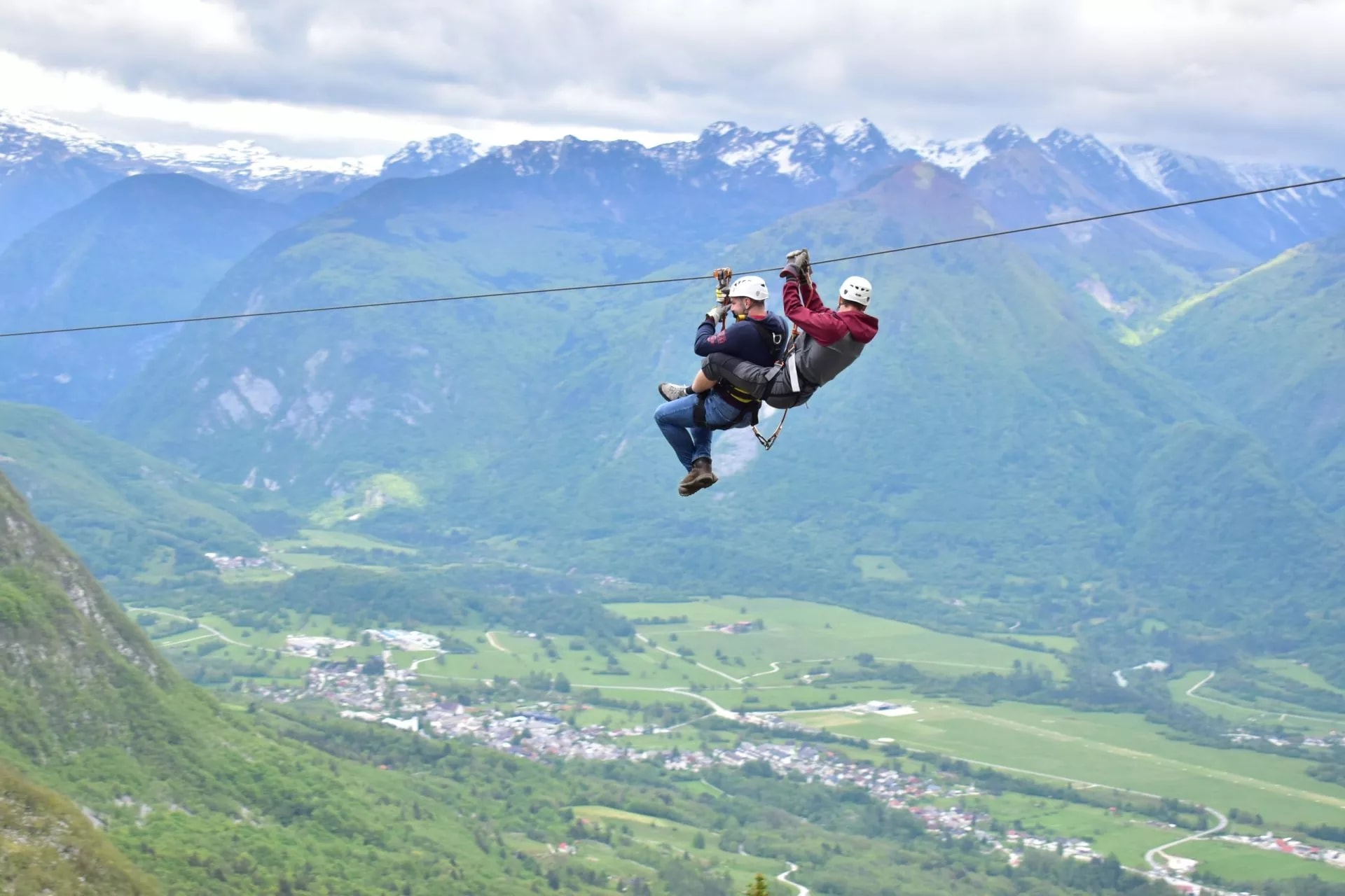 Ziplining over Soca Valley with green slopes and snow-capped mountains in background