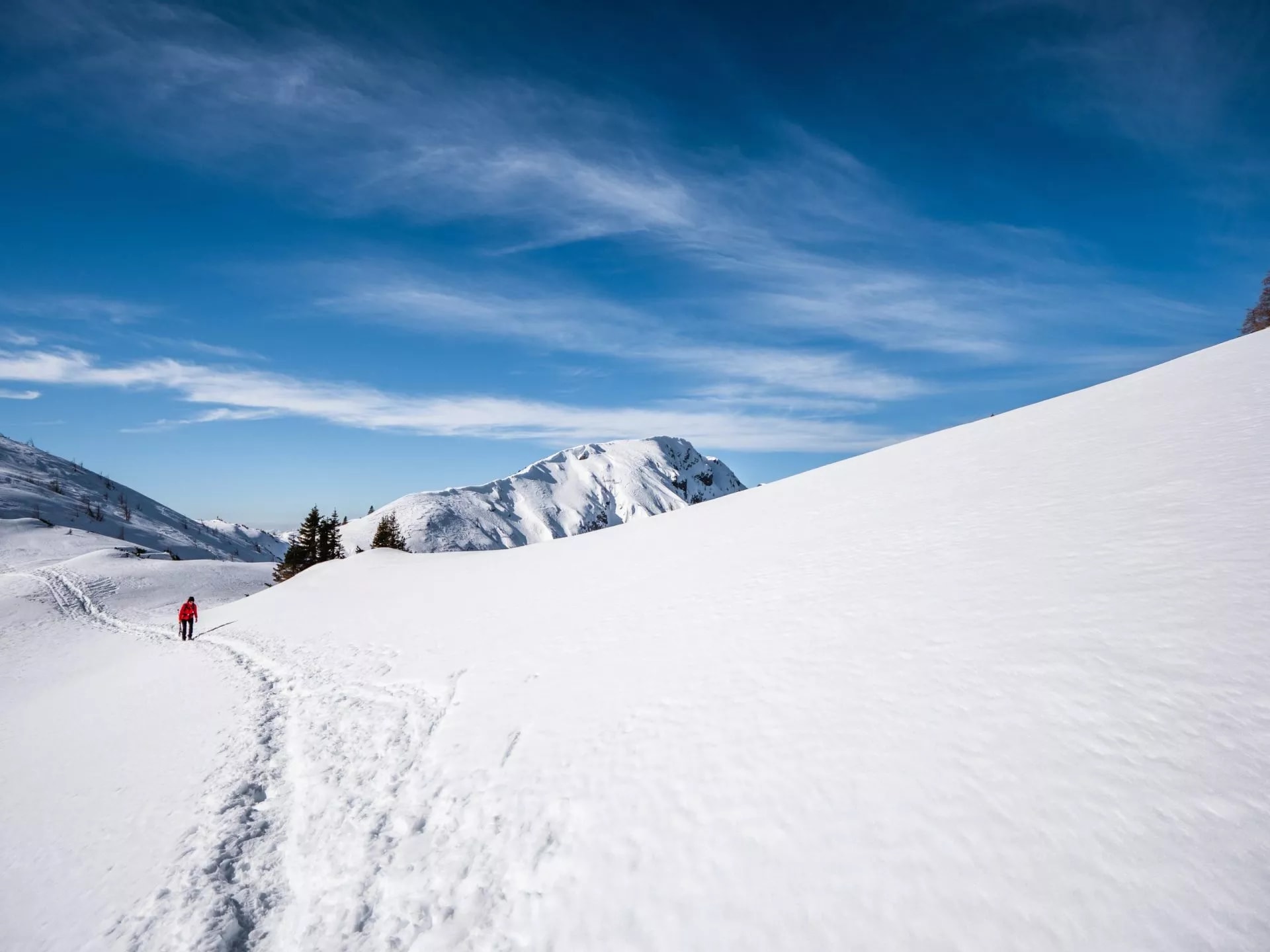 Hiker on snowy path with Triglav National Park mountains under blue sky