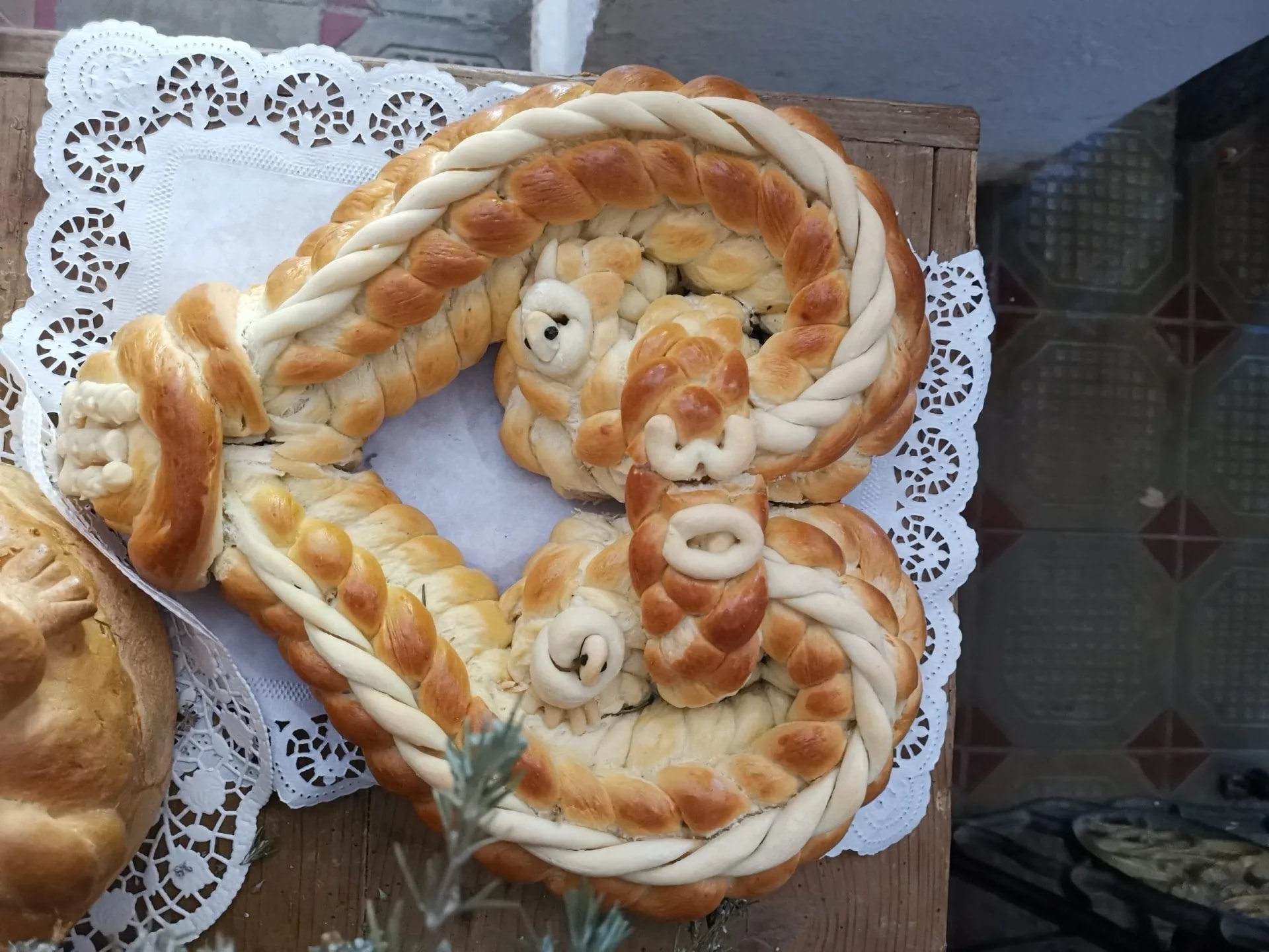Ornate braided ceremonial bread on a white paper doily on a wooden surface.