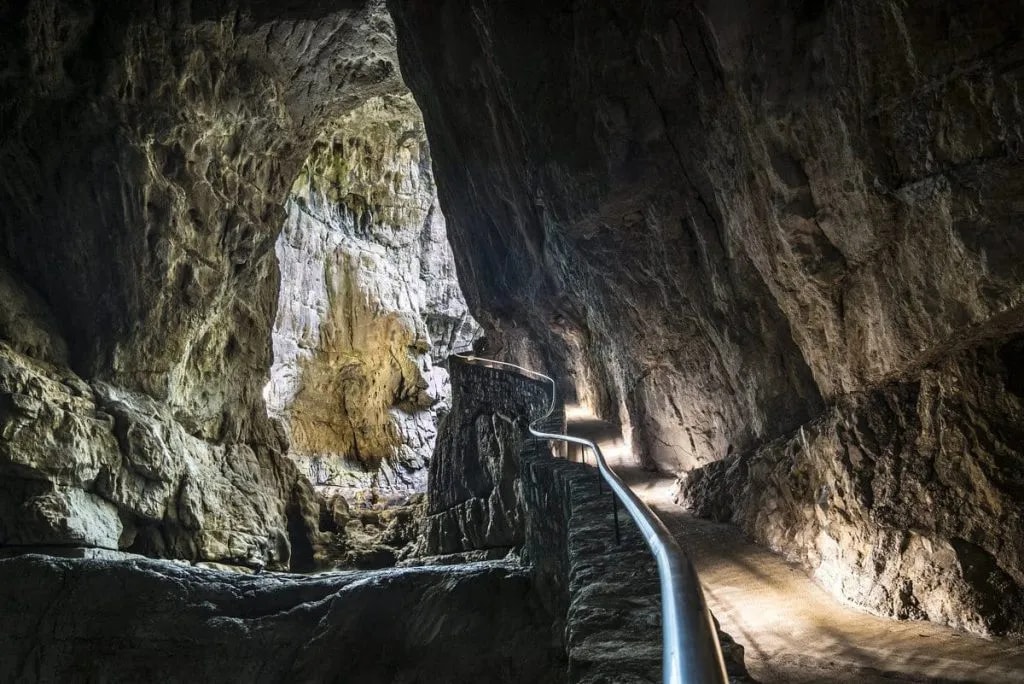 Pathway with metal railing winding through the illuminated interior of Skocjan Caves.