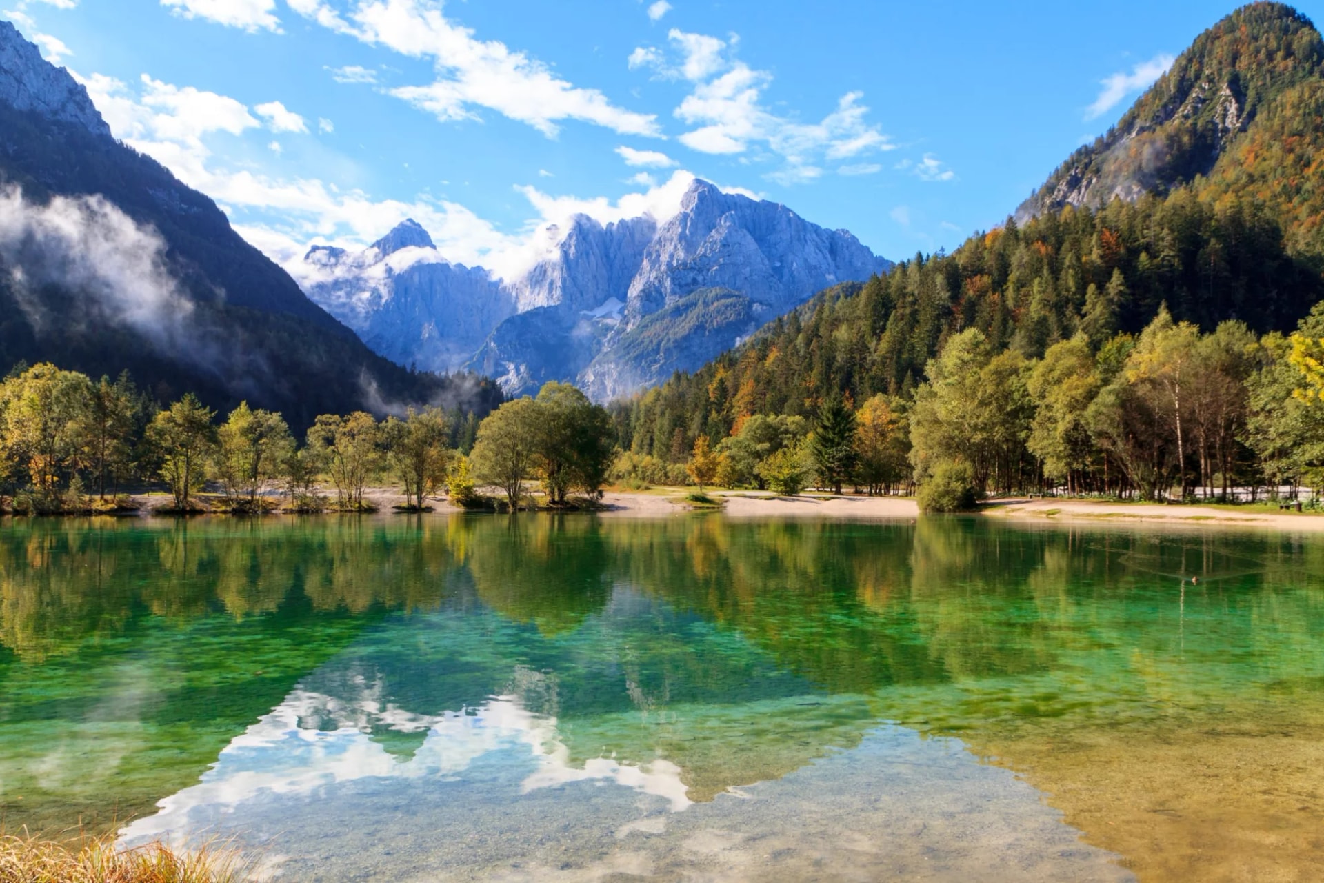Jasna Lake at Kranjska Gora, Slovenia, with clear green water reflecting mountains and autumn trees.