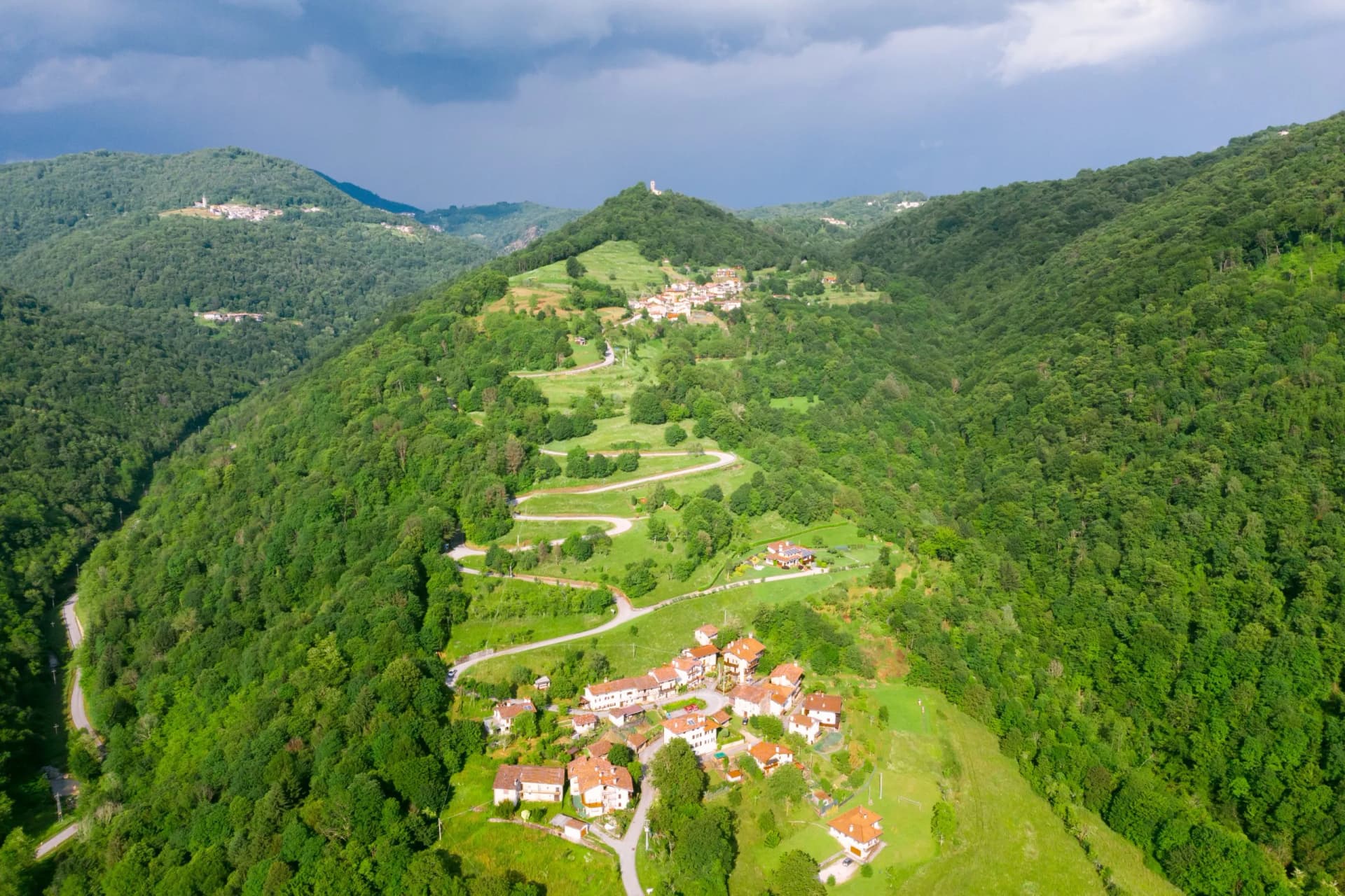 Village of Stregna nestled in lush green mountains with winding roads under a cloudy sky.
