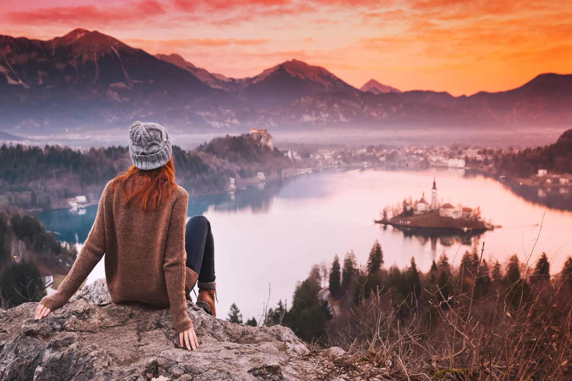 Young woman looking at sunset over Lake Bled with island church and mountains