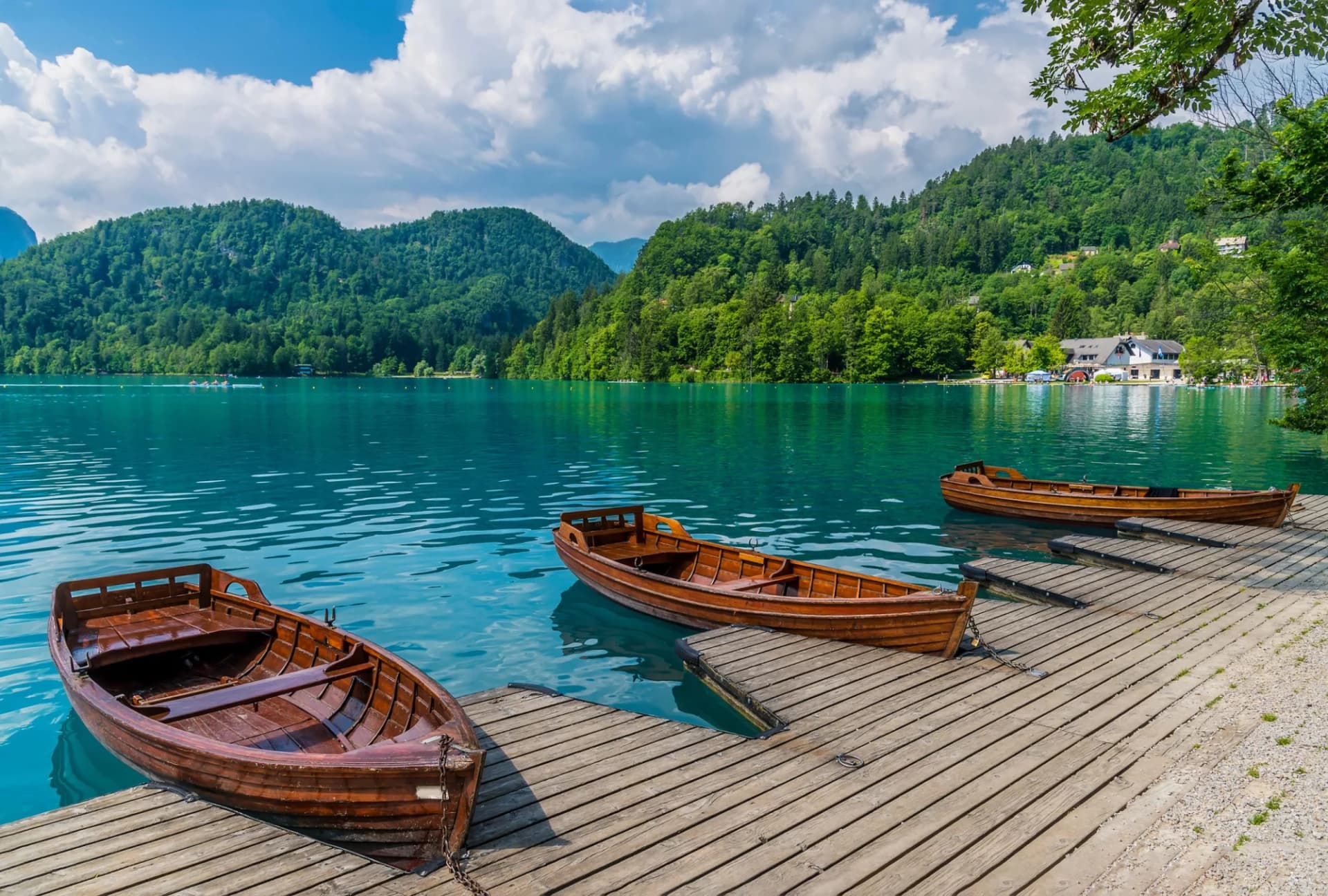 Wooden boats moored at a dock on Lake Bled with lush green mountains under a blue sky.