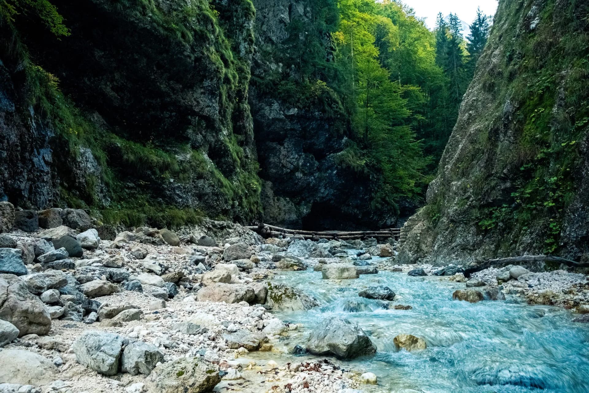 Martuljek waterfalls in Triglav National Park with turquoise stream flowing over rocks and steep mossy cliffs.