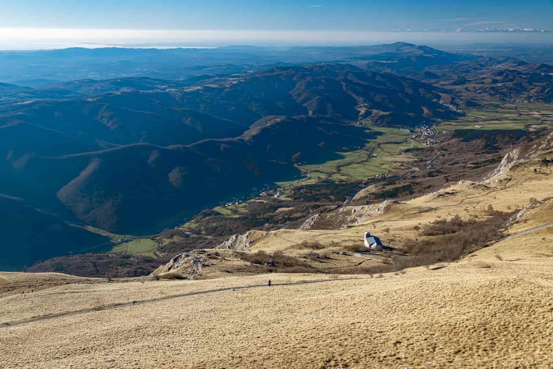 View from Nanos Mountain over Vipava Valley with stone church and distant hazy mountains.