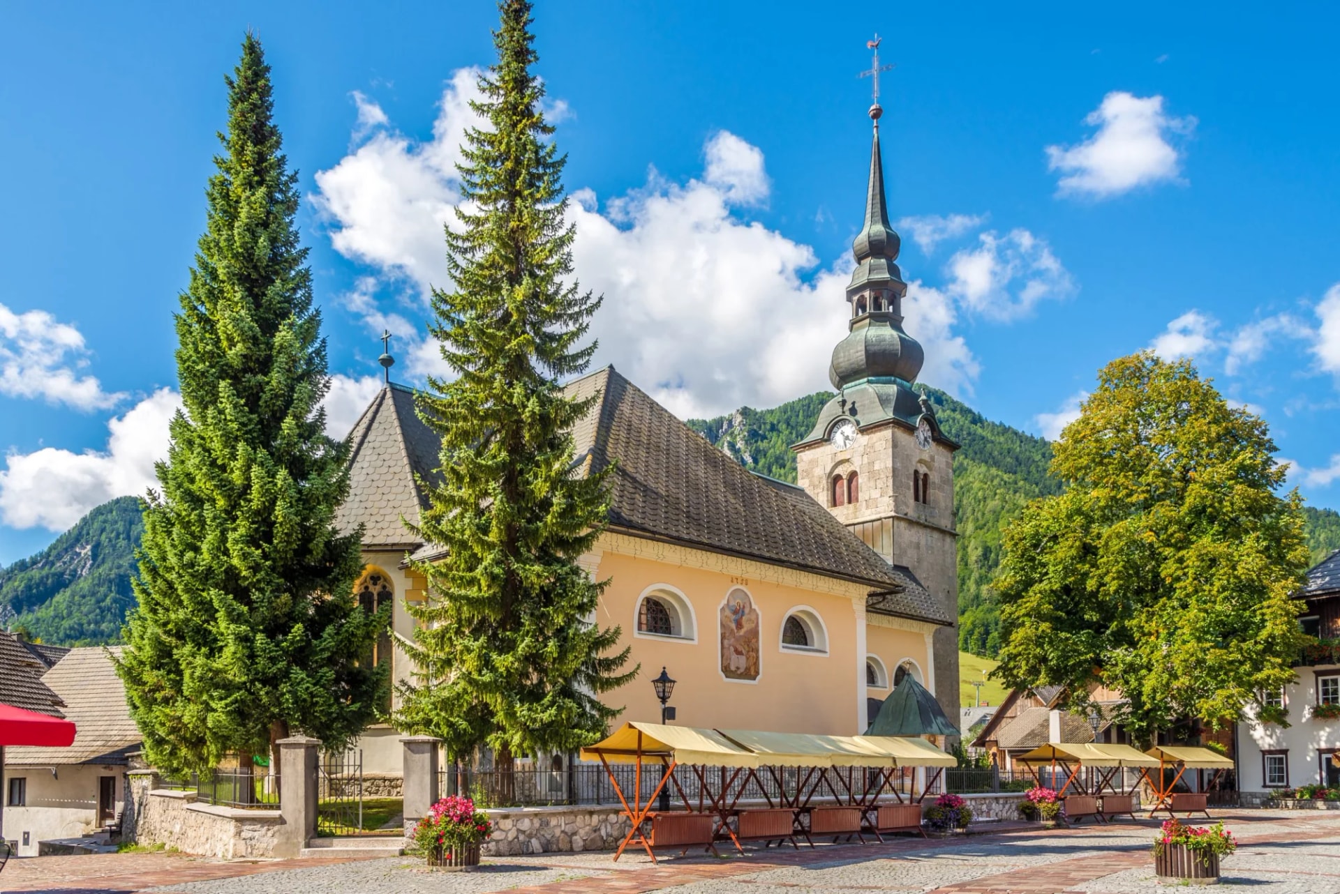 Church of Our Lady on the White Gravel in Kranjska Gora with tall trees and mountains.