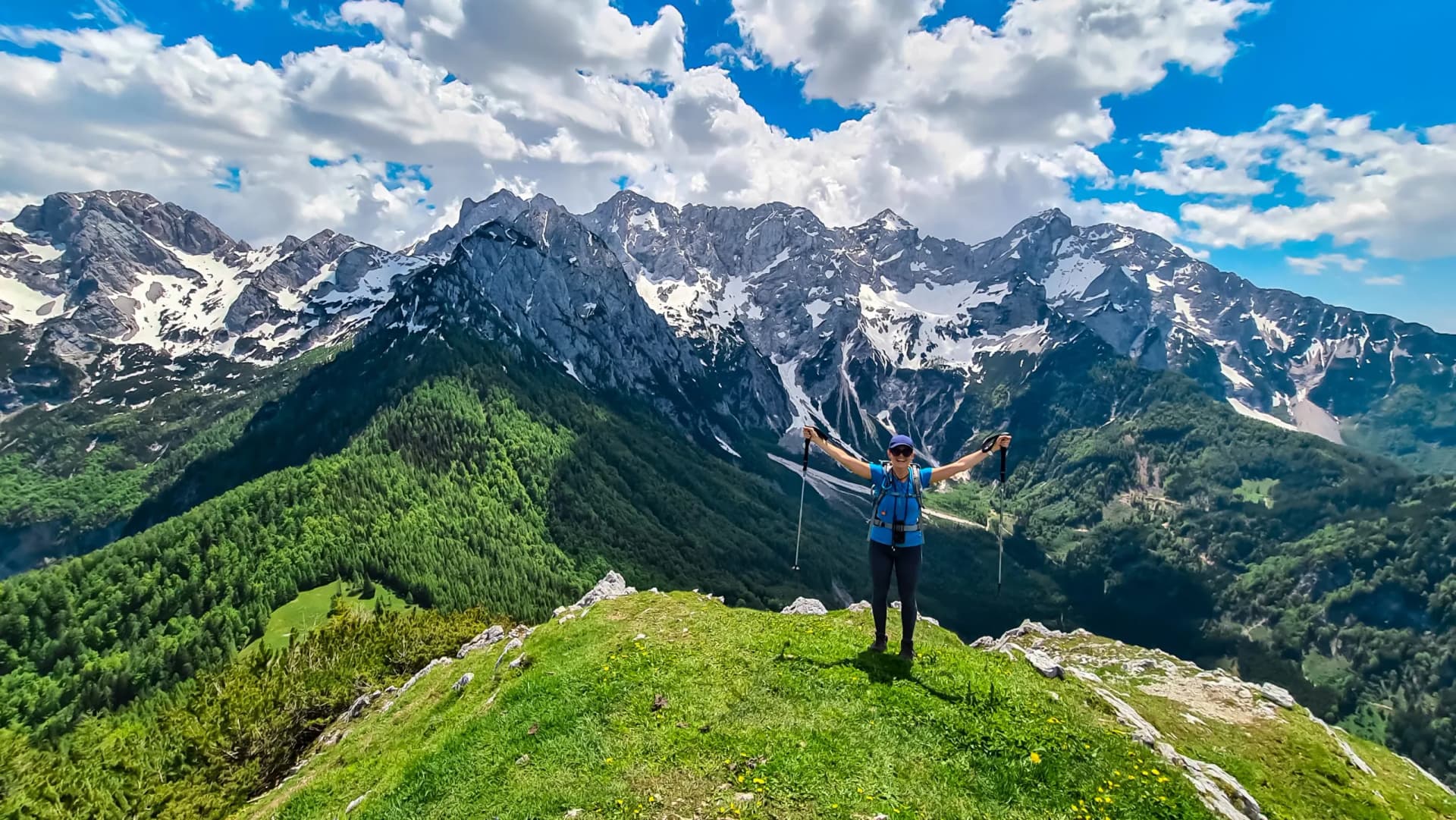 Hiker with arms spread on Goli Vrh summit overlooking Kamnik-Savinja Alps mountains.