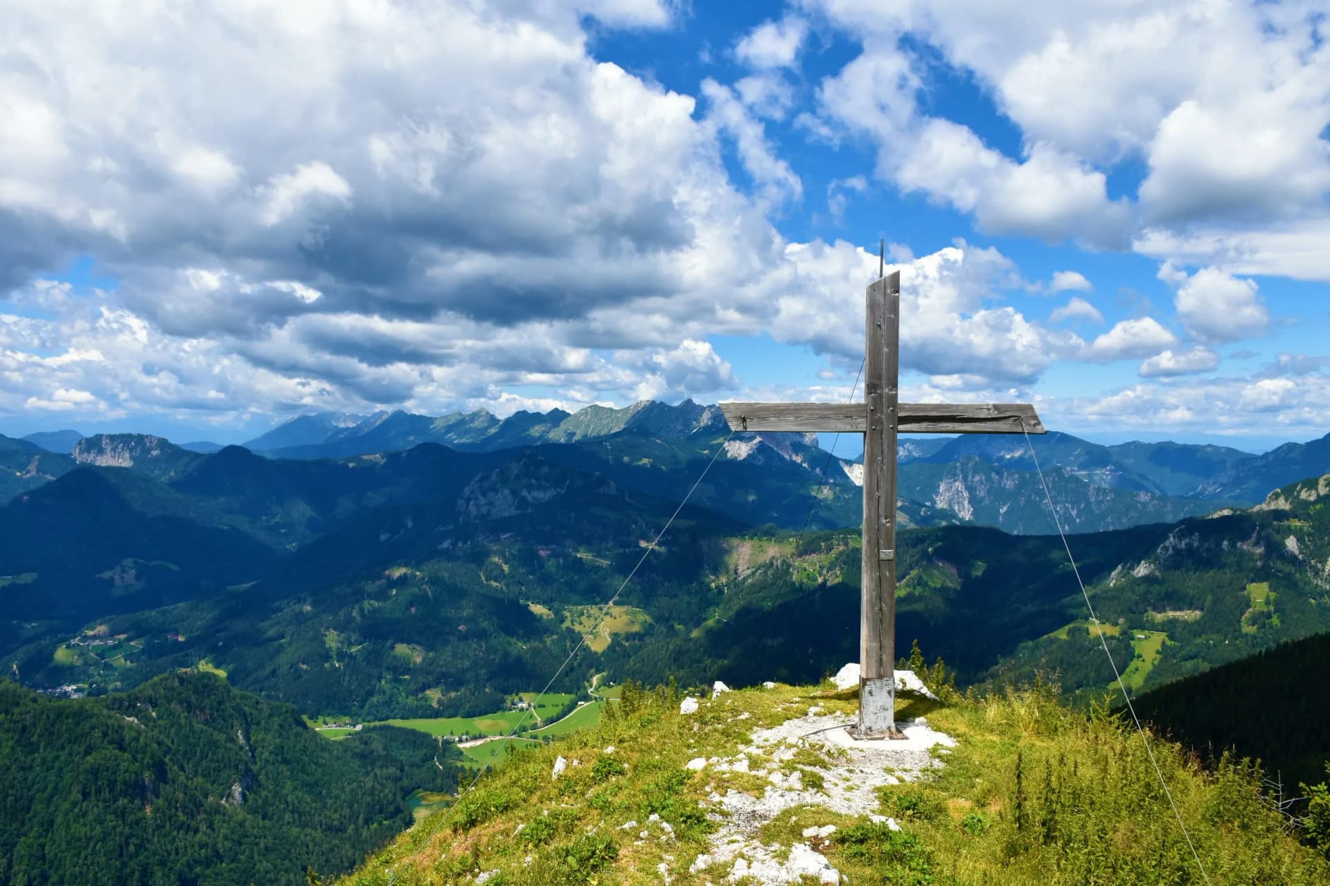 Wooden summit cross on Goli Vrh above Jezersko, Slovenia, overlooking green mountains and clouds.