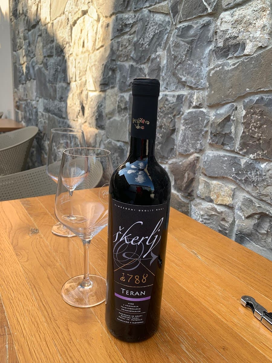 Bottle of Škerlj Teran wine and two empty glasses on wooden table outdoors